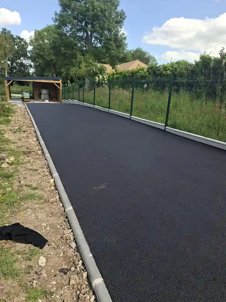 Longue allée en enrobé bordée d'une clôture rigide