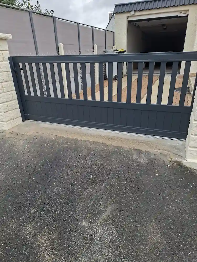 Portail coulissant en aluminium ajouré anthracite devant une allée en enrobé